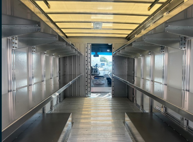 Package A All Fixed shelving in a Workhorse W56 step van, looking forward down the aisle at full-length fixed aluminum shelves on both walls.